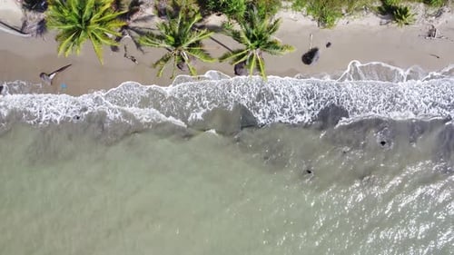 Luftaufnahme der Meereswellen, die bei Sonnenaufgang auf einen wunderschönen Strand mit rosafarbenem Sand rollen