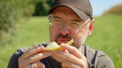 Homme barbu mangeant du melon juteux avec une expression concentrée et un comportement détendu, mâle mordant une tranche de melon