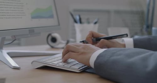 Nahaufnahme weiblicher Hände, die mit der Computertastatur tippen und in ein Notizbuch am Schreibtisch im Büro schreiben