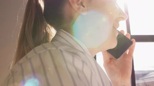 Smiling woman talks on smartphone near window