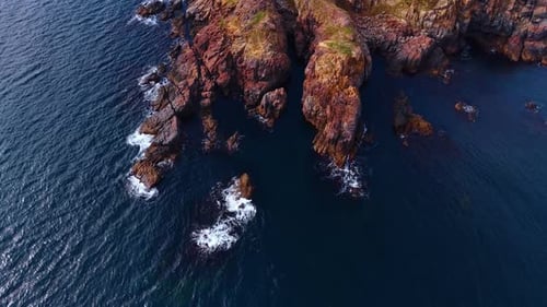 Waves hit the rocky coastline as cliffs rise from the water.