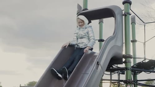 A Tenyearold Girl Slides Down a Children's Slide on a Playground in the Park