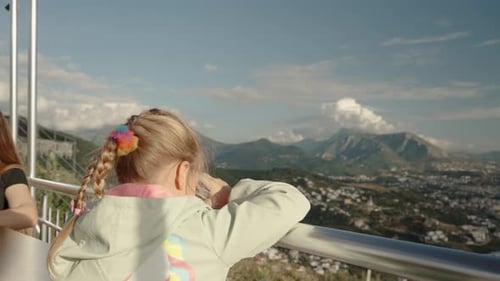A Little Girl on a High Mountain Looking Through Binoculars at the City below, with Mountains
