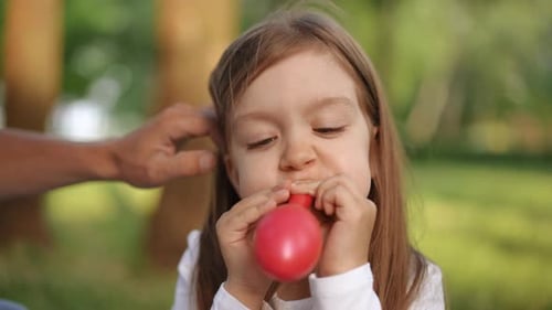 Cute Child Blowing up Red Balloon Outdoors