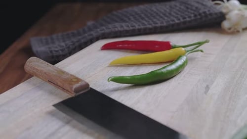 Close up view: Red, yellow and green hot chilis with green onions and knife on board.