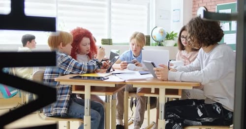 Kluge kaukasische Kinder und Jugendliche, Mädchen und Jungen, die am Schreibtisch sitzen und zusammen in der Schule lernen