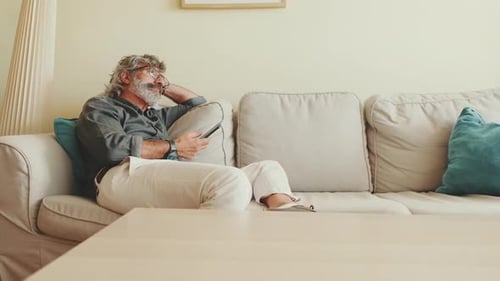 Mature Adult Relaxing with Mobile Phone on Sofa