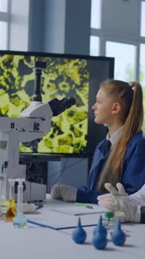 Teen and Woman at Microscope in Laboratory Setting