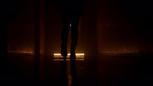 Silhouette Woman Walks Along a Dark Corridor Shooting From a Low Point Orange Light