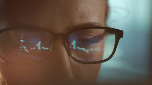 Trader Wearing Glasses is Working on Laptop Computer Screen with Stock Market Charts and Bitcoin BTC