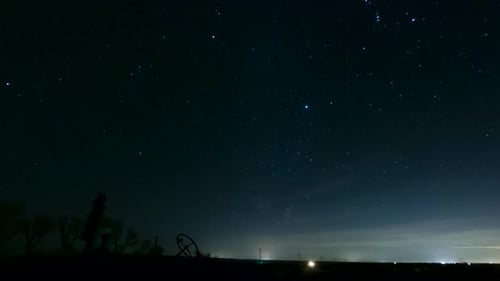 The silhouette of rusted tractor marks the horizon as the heavenly stars cross the night sky - time