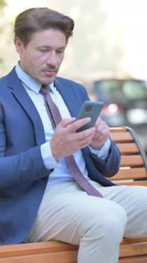 Well-Dressed Man Sits on Bench Using Smart Phone