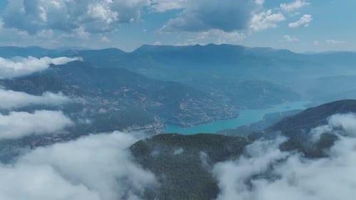 Vista aérea: paisaje montañoso nublado con bosques verdes y extensos campos abiertos
