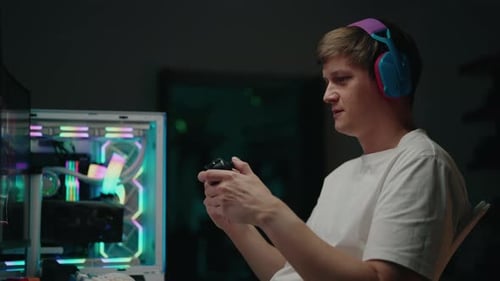 Side View of Focused Gamer Male Playing Latenight Video Game Holding Gamepad and Wearing Headphones