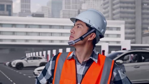 Close Up Of Male Engineer Looking Around With Arms Akimbo, Cars Charging at Station