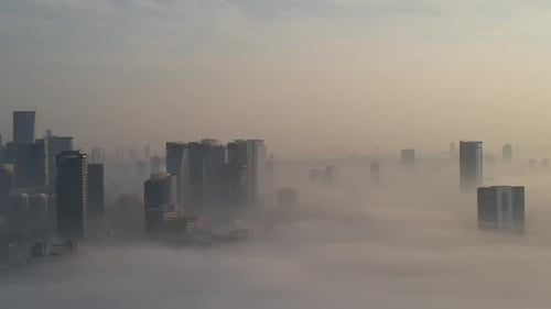 Aerial shot of fog covering buildings in the city, a drone flies sideways in front of residential bu