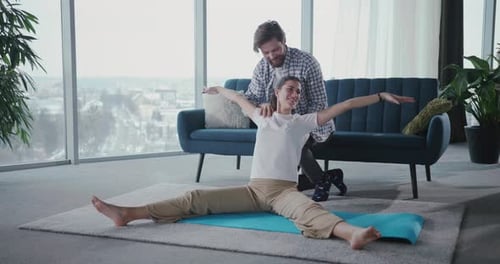 Joven barbudo que ayuda a su novia a hacer ejercicios de estiramiento de yoga en la parte inferior de la espalda practicando