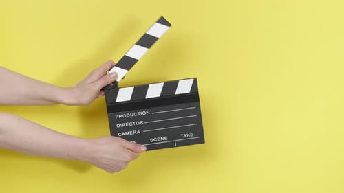 Hands Holding Clapperboard Against a Yellow Background
