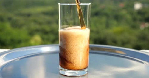 Cola is poured into a glass with ice against the background of a green summer forest. Slow motion.