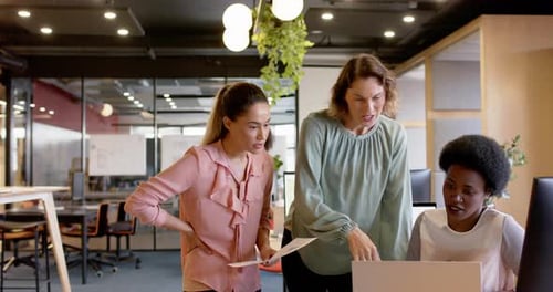 Happy diverse businesswomen discussing work and using laptop at desk in office, in slow motion