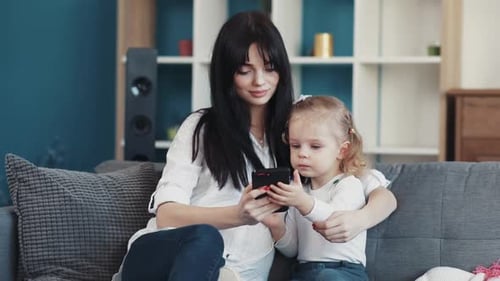 Mother and daughter sitting on sofa using phone