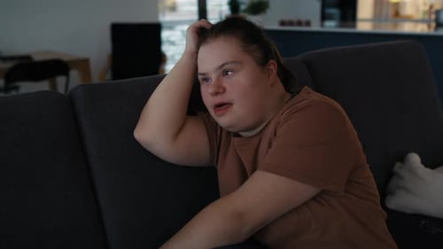 Femme trisomique attentionnée assise sur le canapé et regardant ailleurs. Tourné avec une caméra à hélium ROUGE en 8K
.