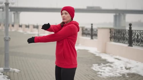 Woman Stretching Outdoors in Winter Near Bridge and Fence