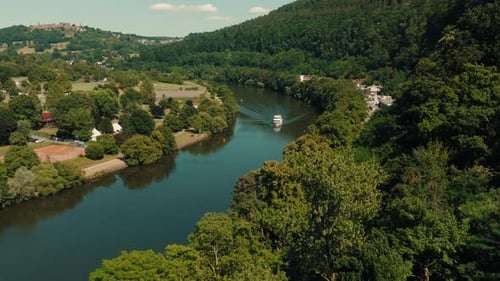 Aerial view flying close to treetops toward cruise ship sailing in calm river canal with natural gre