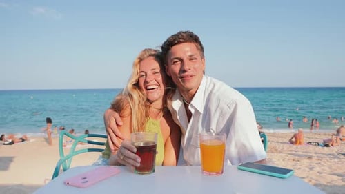 Joyful Couple Enjoying Refreshing Drinks at a Sunny Beach Terrace with Stunning Ocean Views While