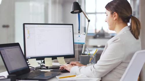 Female programmer working at her desk writes script in a modern technology office
