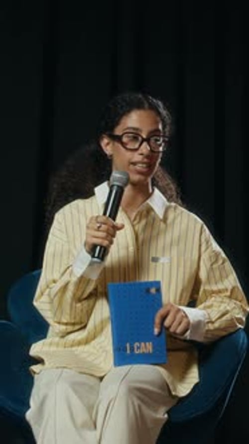 Vertical of Young Female Author Speaking into Mic during Book Conference