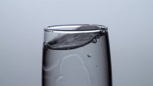 Close Up Of Ice Cube Falling In A Glass Of Drinking Water On White Background