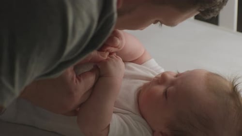 Father Kisses Newborn Baby Arms in Crib