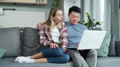 Happy young married couple shopping online choosing a product in online store together on laptop