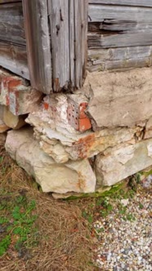 Vertical close-up of a decayed building corner with crumbling stone foundation, exposed brick, and