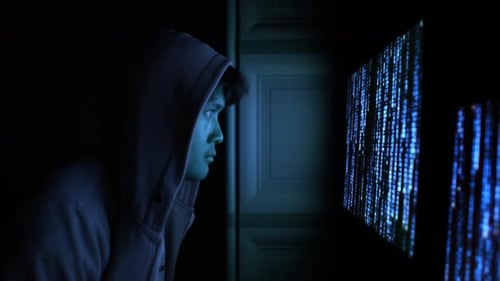 Hooded Hacker illuminé par un écran de code informatique bleu