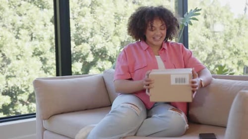 Opening package, woman sitting on couch and smiling, enjoying delivery