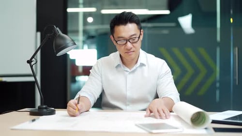 Asian creative designer or architect working in the office at work at a computer desk with drawings.
