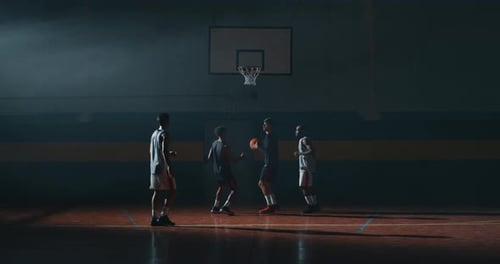 Young Men Playing Basketball in Dark Indoor Court