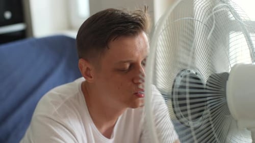 Man Cooling Off Indoors in Front of a Fan