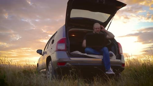 Freelancer atencioso e preocupado trabalhando no laptop Homem digitando no teclado sentado no porta-malas do carro