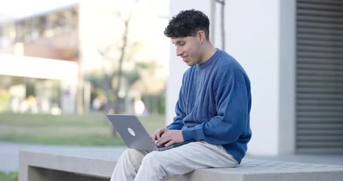 Young Adult Using Laptop Outdoors on Bench