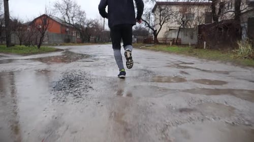 Beine eines jungen Sportlers, der an einem Regentag auf einem ländlichen Pfad läuft Männliche Füße eines sportlichen Läufers beim Joggen