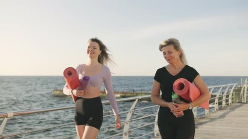 Two Women Walking By the Ocean Carrying Yoga Mats and Enjoying a Sunny Day