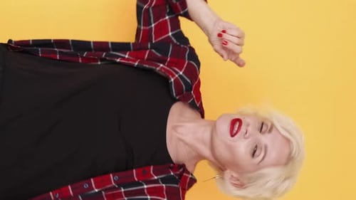 Stylish Senior Woman Dancing Joyfully on Yellow Background