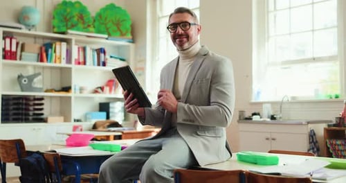 Smiling man holds tablet sitting in school classroom