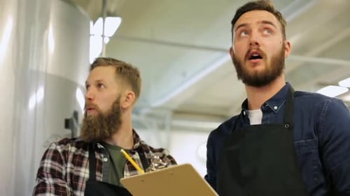 Two men inspect the brewery tanks inside factory
