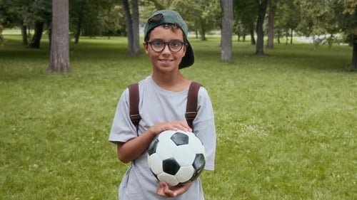 Portrait of Positive Twelve-Year-Old Boy Holding Soccer Ball in Park