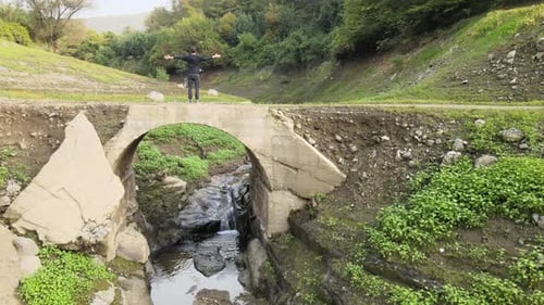 Man Stands on Old Bridge Above River