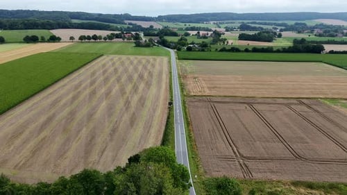 Main Street surrounded by agricultural farm fields and hills on cloudy summer day. American rural su